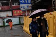 People wearing face masks walk next to barricades set up at a residential area in Wuhan