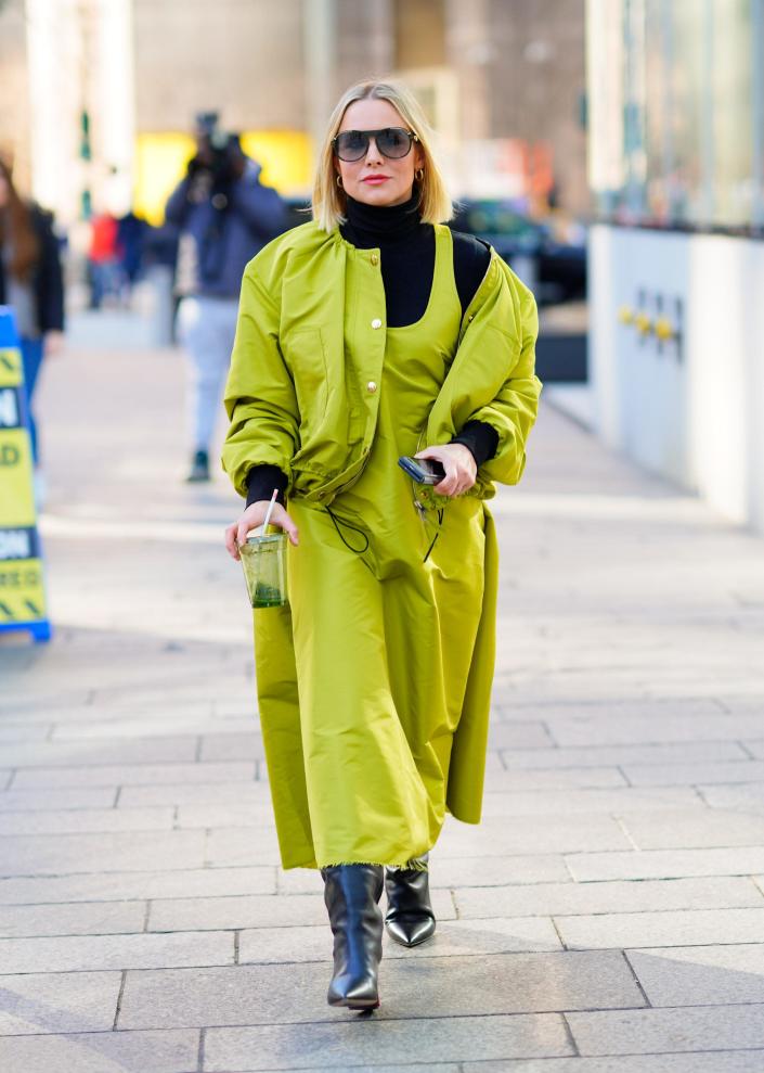 Kristen Bell in a neon green coat and black boots walking down the street