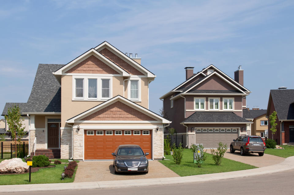 Two suburban houses with manicured lawns and a car parked in the driveway of one