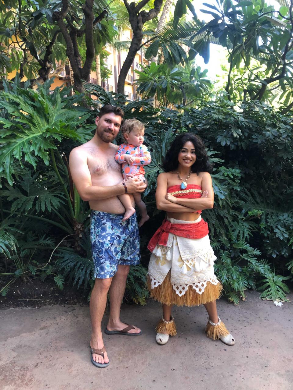 A man holding his baby posing with the Disney character, Moana.