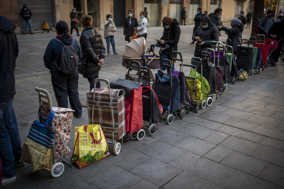 Shopping trollies lined up next to their owners, waiting their turn to receive a weekly pack of donated food and supplies, outside a church in Barcelona, Spain, Wednesday, Feb. 3, 2021. Food requests have increased considerably in the last months as Spain has been in lockdown due to the coronavirus pandemic. (AP Photo/Emilio Morenatti)