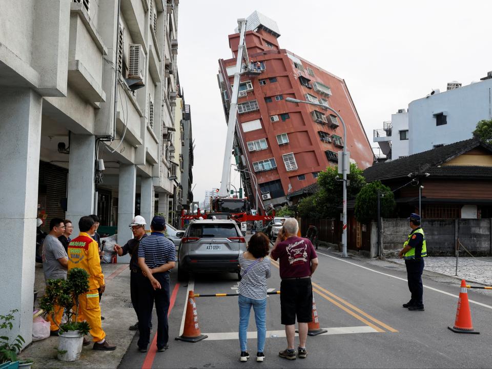 People look on as workers carry out operations while on an elevated platform of a firefighting truck at the site where a building collapsed (REUTERS)