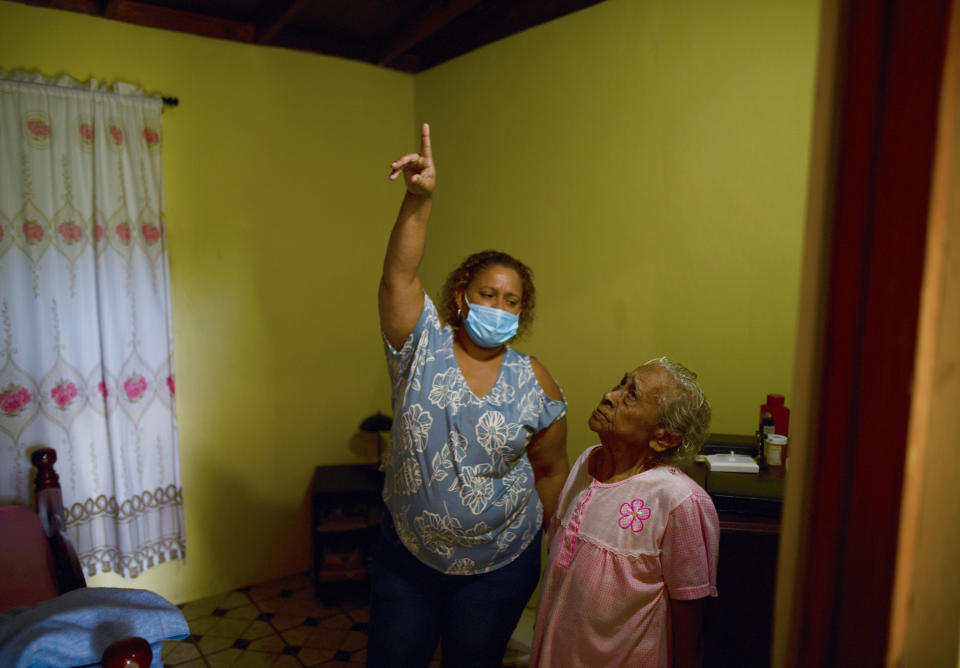 Maria Matilde Parrilla, 92, right, looks up as a municipal worker points a faulty joint in her wood and zinc roof, in Loiza, Puerto Rico, Thursday, May 28, 2020. Caribbean islands have rarely been so vulnerable as an unusually active hurricane season this year threatens a region still recovering from recent storms as it fights a worsening drought and a pandemic that has drained budgets and muddled preparations. (AP Photo/Carlos Giusti)