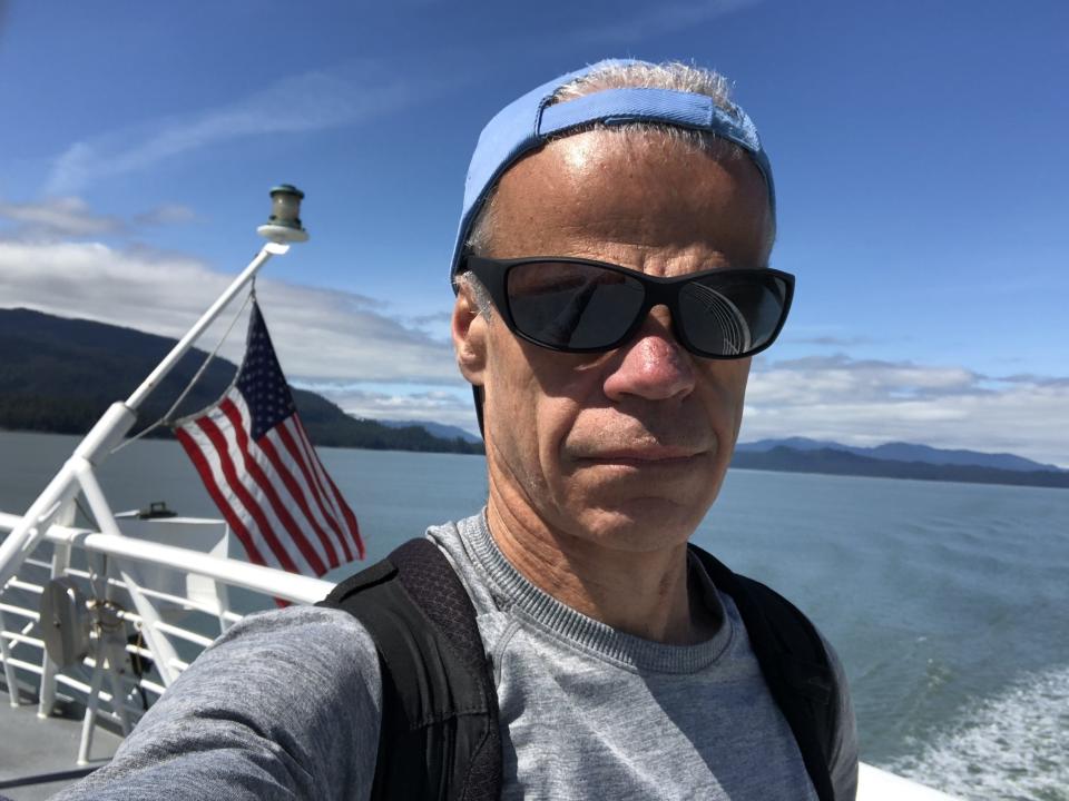 A man with a backwards hat taking a selfie on a ship on the water.