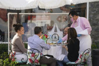 Diners are served outside by a waiter wearing a mask, face shield and rubber gloves, Wednesday, Nov. 18, 2020, in West Hollywood, Calif. Los Angeles County imposed new restrictions on businesses Tuesday and is readying plans for a mandatory curfew for all but essential workers if coronavirus cases keep spiking. (AP Photo/Ashley Landis)