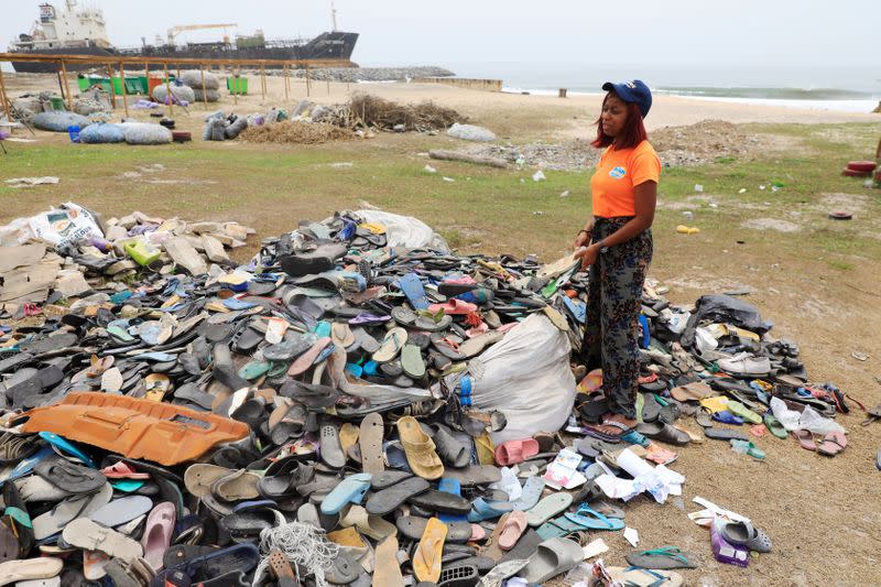 An Environmentalist, Doyinsola Ogunye stands in front of a heap of footwear picked from the shore at the beach in Lagos