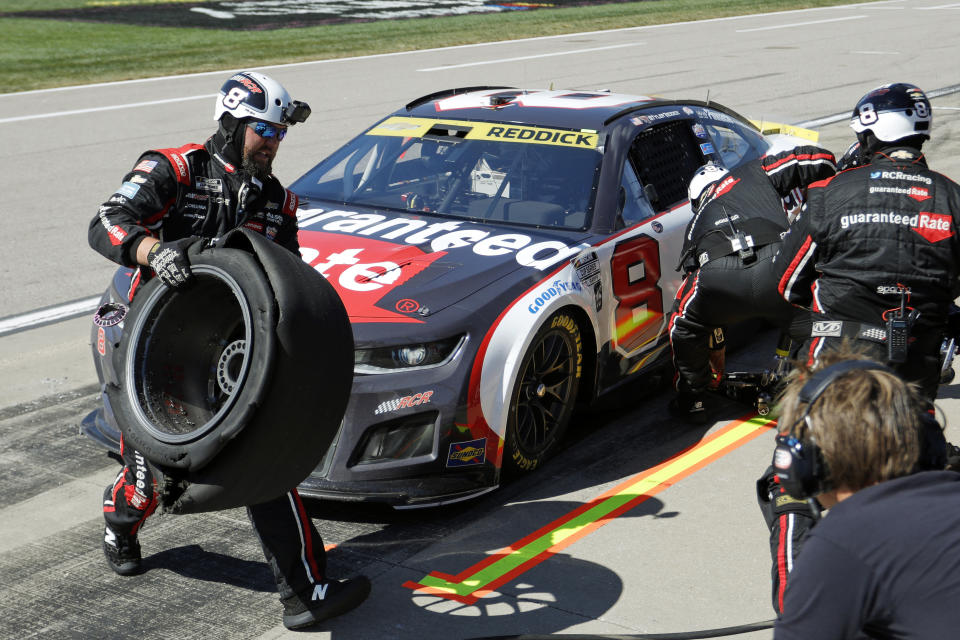 A crew member for Tyler Reddick's No. 8 car, left, carries a damaged tire away during a pit stop at a NASCAR Cup Series auto race at Kansas Speedway in Kansas City, Kan., Sunday, Sept. 11, 2022. (AP Photo/Colin E. Braley)