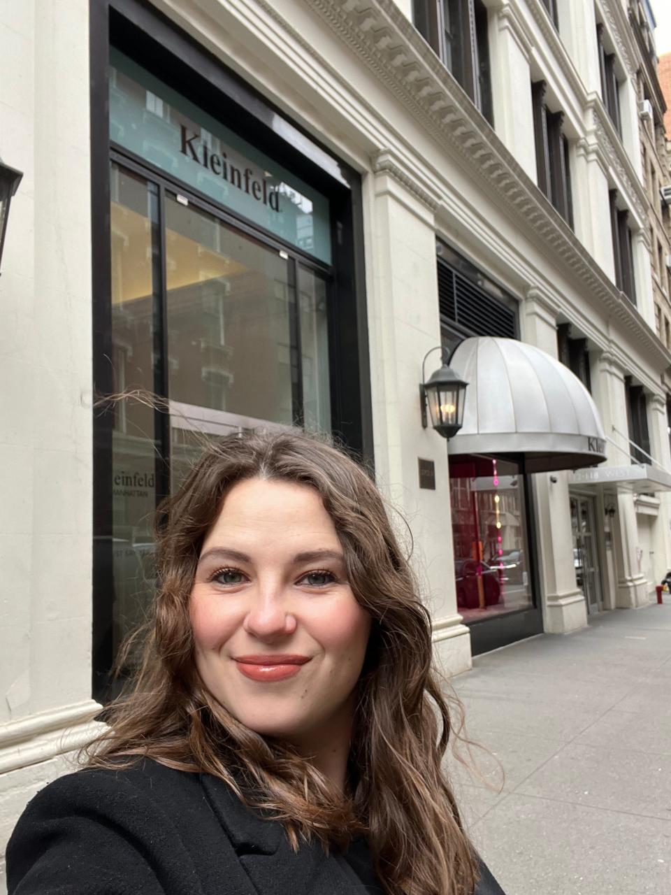 A woman with brown hair poses for a selfie outside of Kleinfeld Bridal.
