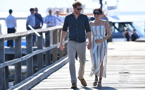 The Duchess of Sussex clutched her baby bump for part of a walk along a jetty in Kingfisher Bay with her husband - Credit: DARREN ENGLAND /AFP