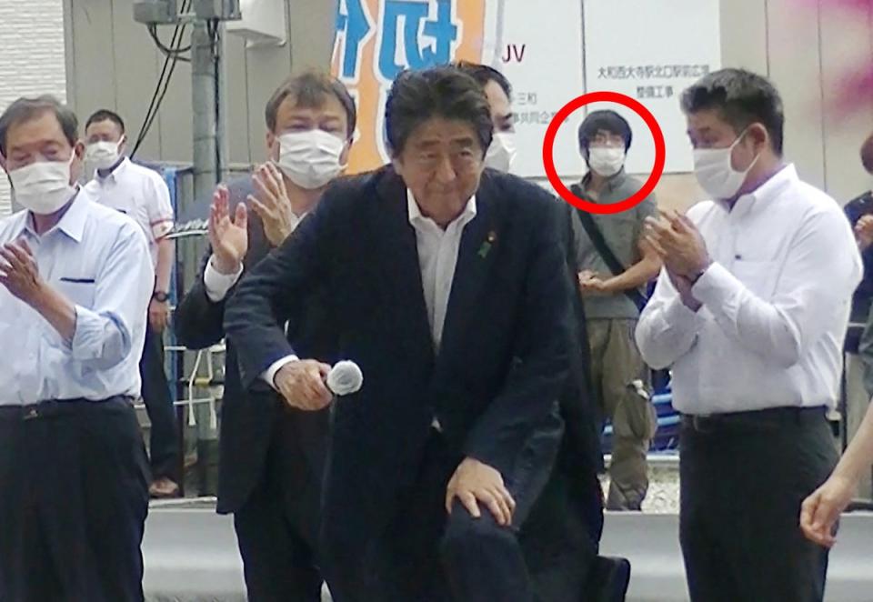 Shinzo attending an election campaign before giving a speech at Kintetsu Yamato-Saidaiji station square in Nara, while a man suspected of shooting Abe shortly after stands in the background (JIJI PRESS/AFP via Getty Images)