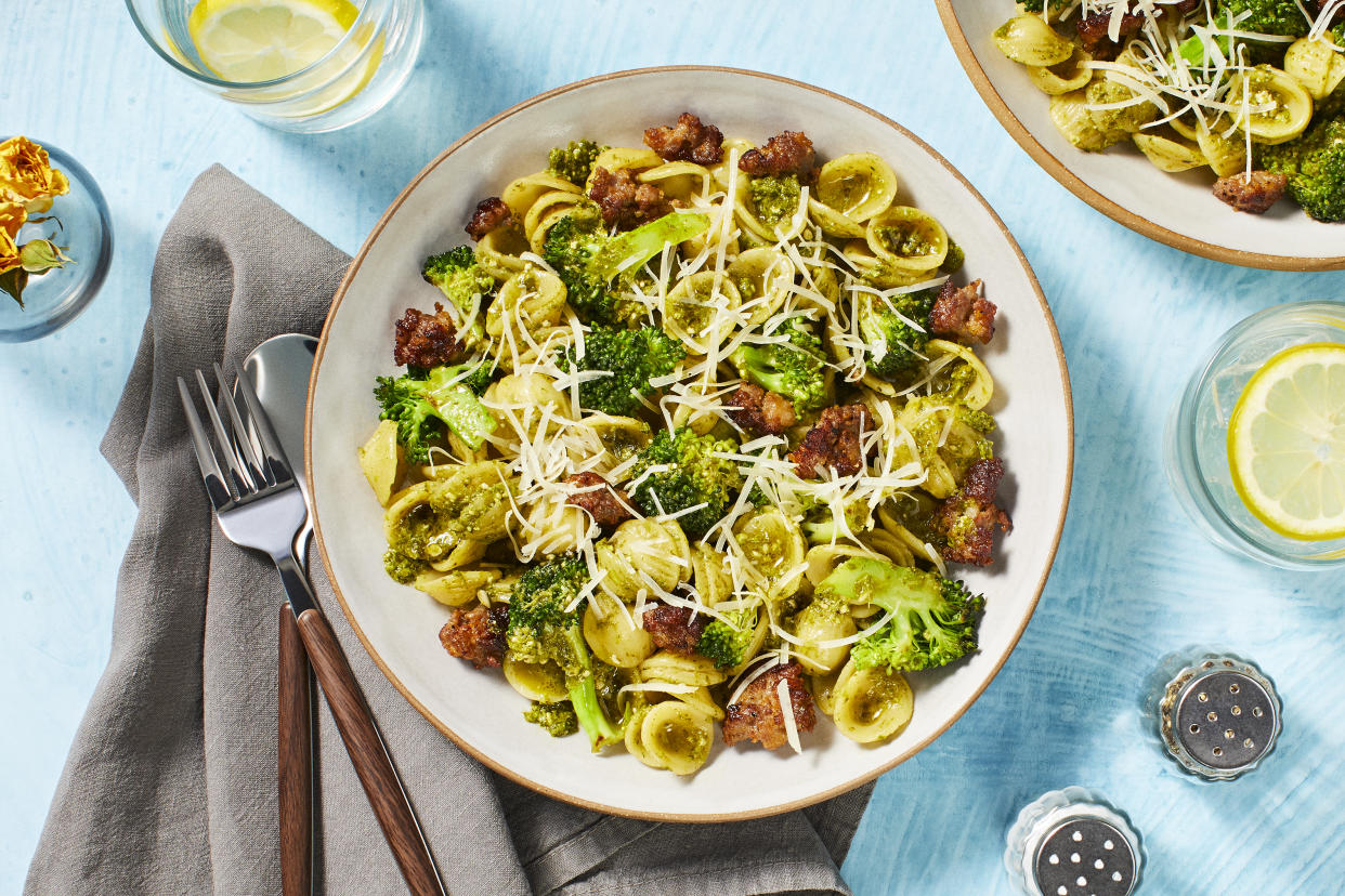 Pasta and broccoli dish on a table with utensils and napkin.