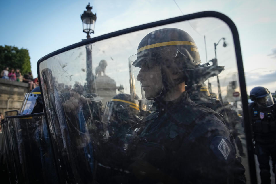 Police officers stand guard in front of protesters on Concorde square during a protest in Paris, France, Friday, June 30, 2023. French President Emmanuel Macron urged parents Friday to keep teenagers at home and proposed restrictions on social media to quell rioting spreading across France over the fatal police shooting of a 17-year-old driver. (AP Photo/Lewis Joly)