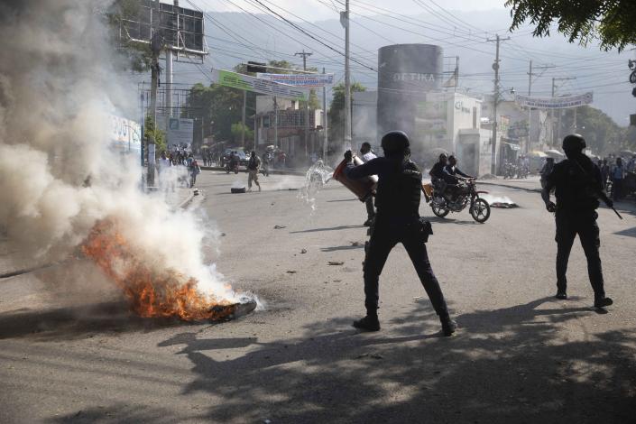 National police work to douse a burning barricade set up by friends and relatives of James Philistin who was kidnapped last night, in Port-au-Prince, Haiti, Wednesday, Nov. 24, 2021. (AP Photo/Odelyn Joseph)
