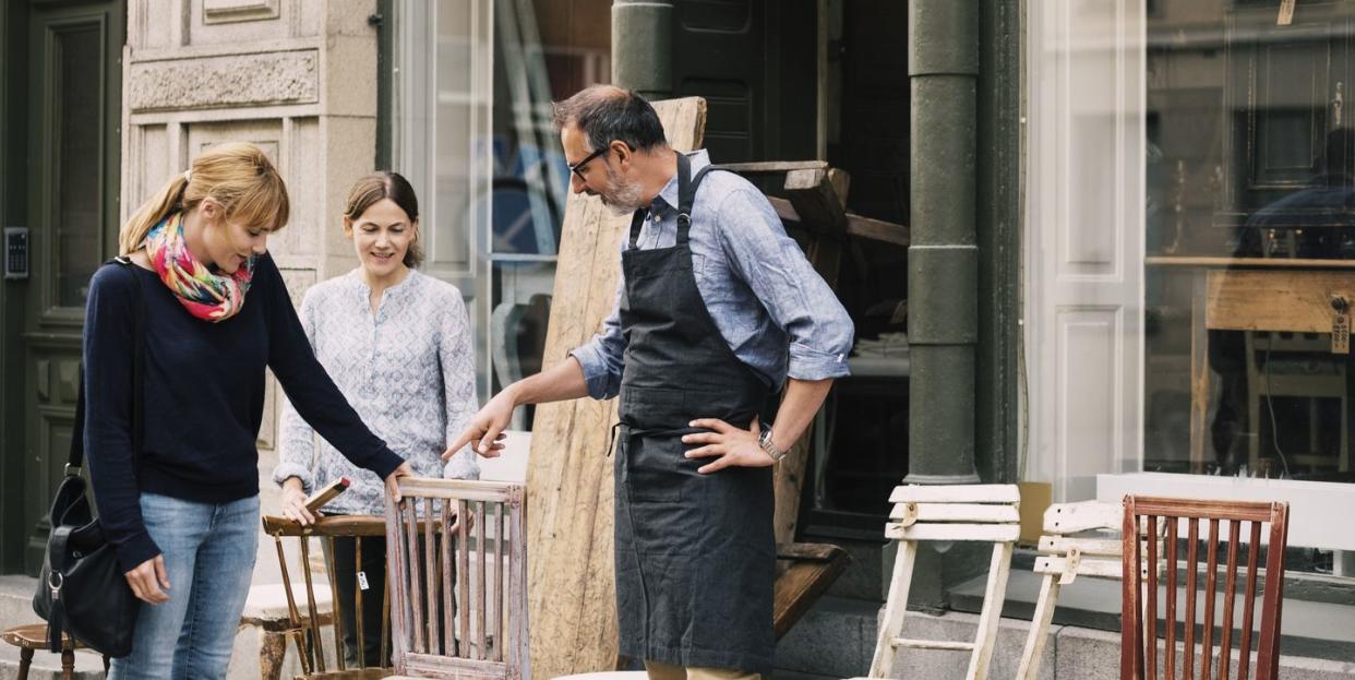 smiling retailers assisting woman outside shop