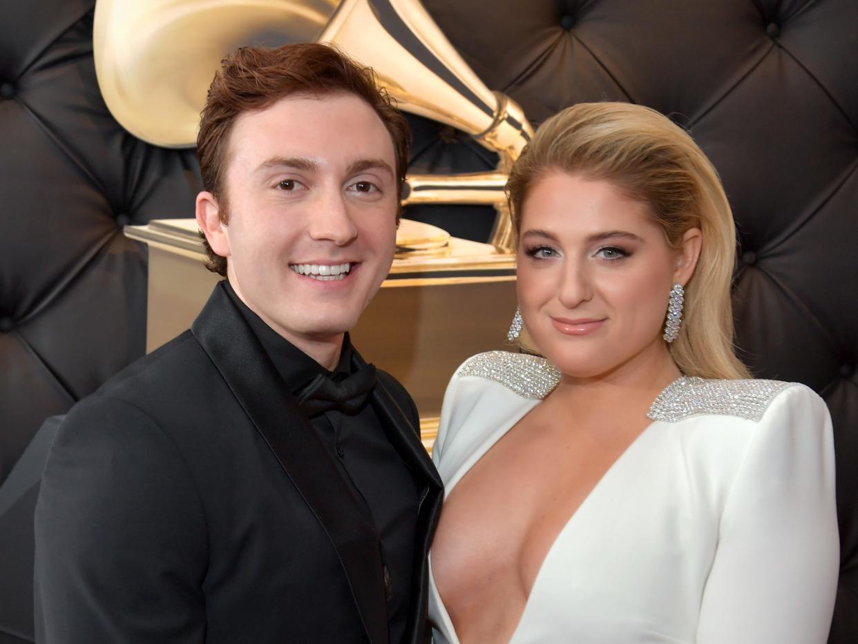 daryl sabara and meghan trainor at the grammys in 2019. sabara is wearing an all black suit and black bowtie, while trainor is in an all white ensemble with a deep v that shows her cleavage, and sparkling accents on the shoulders and waist. her hair is styled away from her face