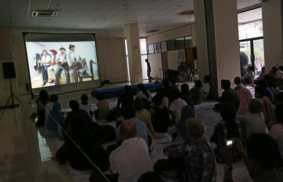 in this Monday, Sept 30, 2013 photo, people gather and watch a documentary film, "The Act of Killing" in Jakarta, Indonesia. The film, which explores the mass killing of communists in 1965, was made free online this week in Indonesia. A new American-directed documentary, "The Act of Killing," challenges widely held views about hundreds of thousands of deaths carried out across Indonesia from 1965 to 1966 in the name of fighting communism. It explores the country’s darkest open secret by allowing former mass killers to re-enact their horrors on screen. (AP Photo/Tatan Syuflana)