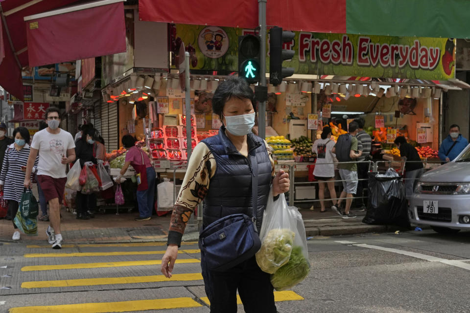 A woman wearing a face mask carries produce across a street in Hong Kong, Sunday, March 13, 2022. The territory's leader, Chief Executive Carrie Lam, warned the peak of the latest surge in coronavirus infections might not have passed yet. (AP Photo/Kin Cheung)