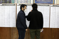 Voters with facemasks confer while checking the list of the candidates in the parliamentary elections in a polling station in Tehran, Iran, Friday, Feb. 21, 2020. Iranians began voting for a new parliament Friday, with turnout seen as a key measure of support for Iran's leadership as sanctions weigh on the economy and isolate the country diplomatically. Also looming over the election is the threat of the new coronavirus, which has been confirmed in five people in Iran this week. (AP Photo/Vahid Salemi)
