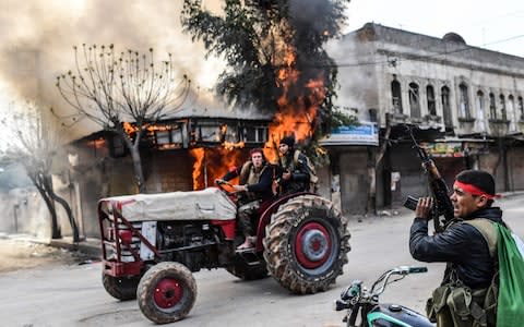  A Turkish-backed Syrian rebel drives past a burning shop in the city of Afrin in northern Syria on March 18 - Credit: BULENT KILIC /AFP