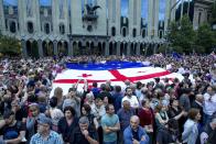 Demonstrators hold huge Georgian, EU and Ukrainian national flags during a rally of Georgian people who want to join the EU, in front of the Parliamentary building in Tbilisi, Georgia, Friday, June 24, 2022. Tens of thousands of people again gathered in the center of Tbilisi. (AP Photo/Shakh Aivazov)