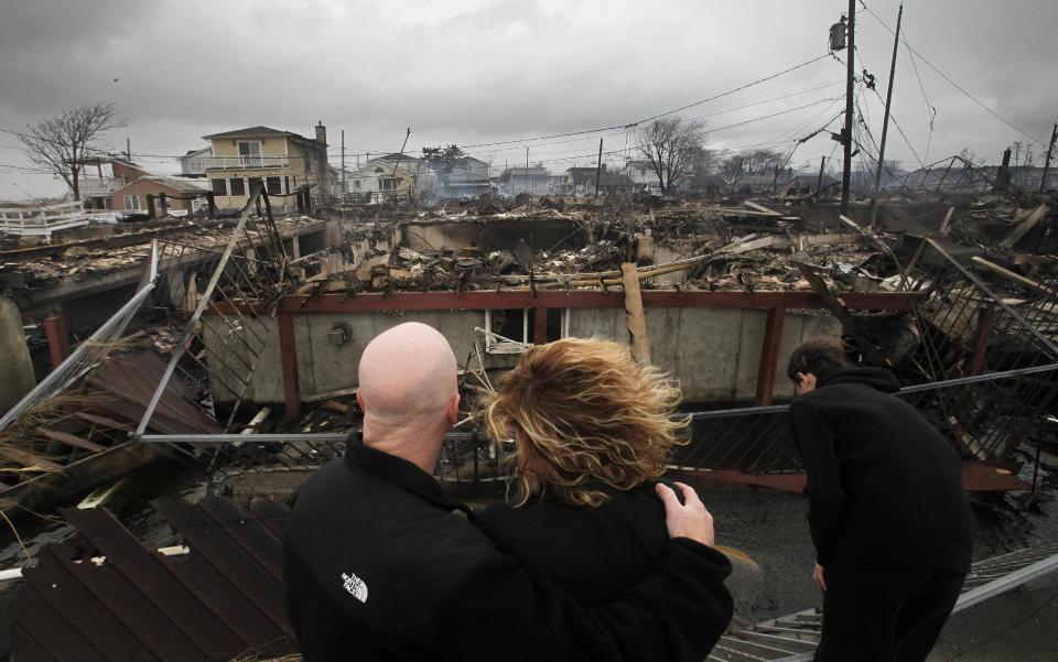 FILE - In this Tuesday, Oct. 30, 2012 file photo, Robert Connolly, left, embraces his wife, Laura, as their son Kyle leans over, at right, as they survey the remains of the home owned by Laura's parents that burned to the ground in the Breezy Point section of New York, following Superstorm Sandy. Sandy ran up a $42 billion bill on New York and the state and New York City are making big requests for disaster aid from the federal government, according to one of Gov. Andrew Cuomo's administration officials. (AP Photo/Mark Lennihan, File)