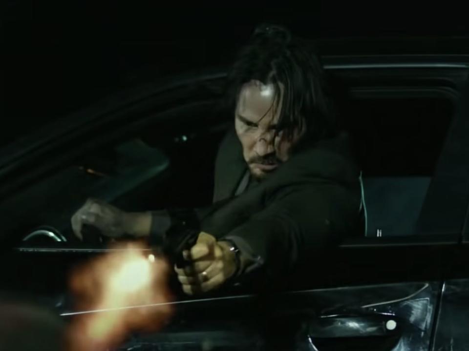 Keanu Reeves as John Wick shooting someone from his car.