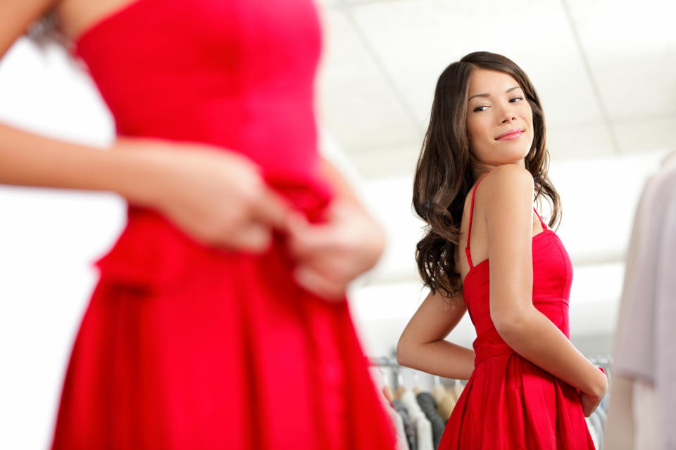 A woman looks at herself in a mirror as she tried on a red dress.