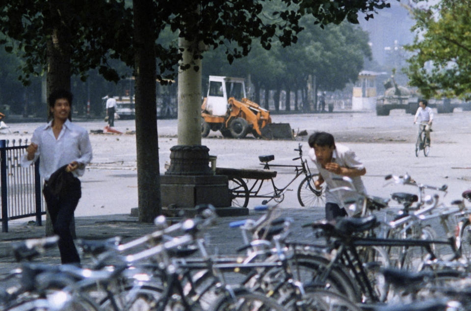 FILE - In this June 5, 1989, file photo, three unidentified men flee the scene, as a Chinese man, background left, stands alone to block a line of approaching tanks, background right, in Beijing's Tiananmen Square. The man in the background stood his ground and blocked the column of tanks when they came closer, an image captured on film by numerous other photographers and one that ultimately became a widely reproduced symbol of events there. (AP Photo/Terril Jones, File)