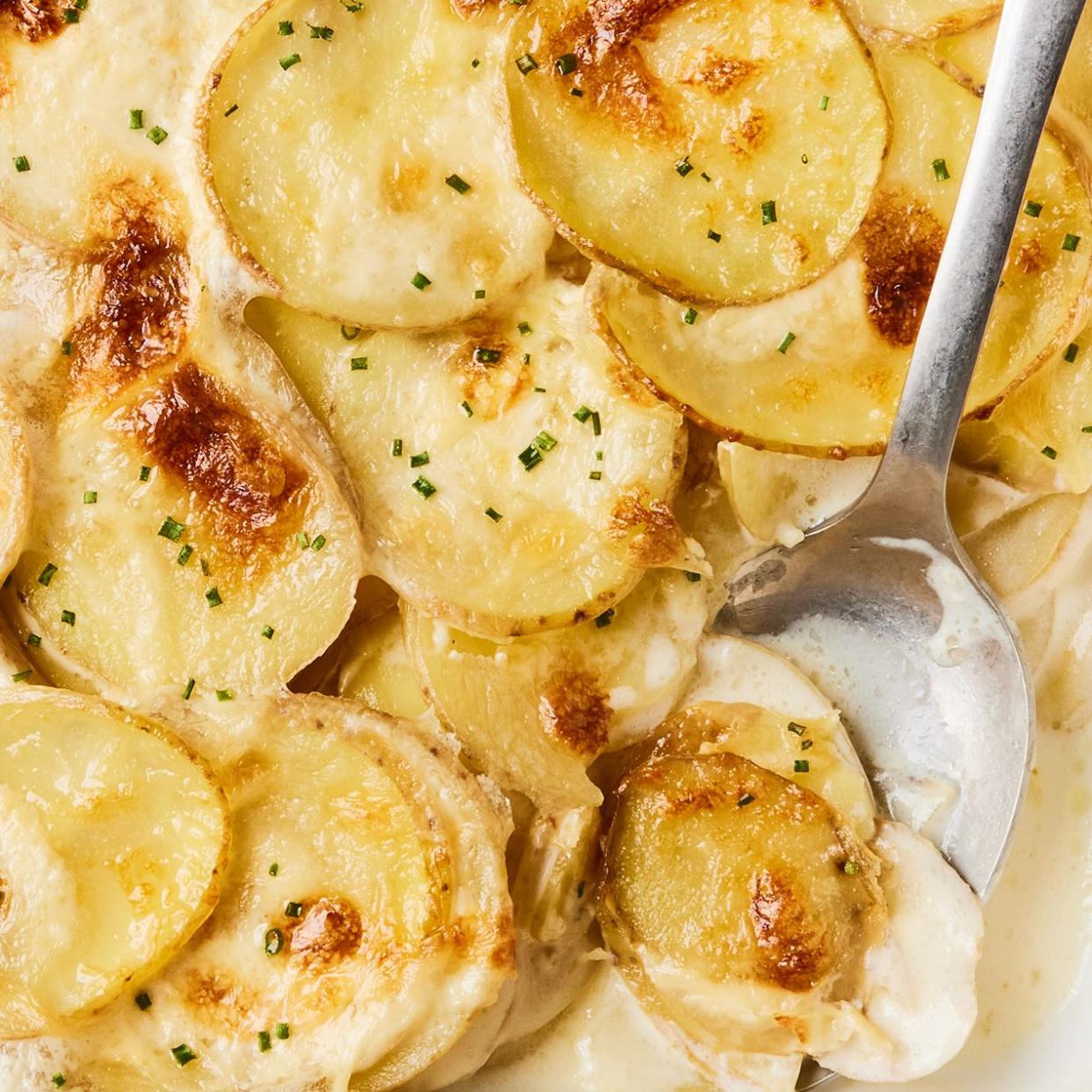 scalloped potatoes in a white baking dish with a silver serving spoon