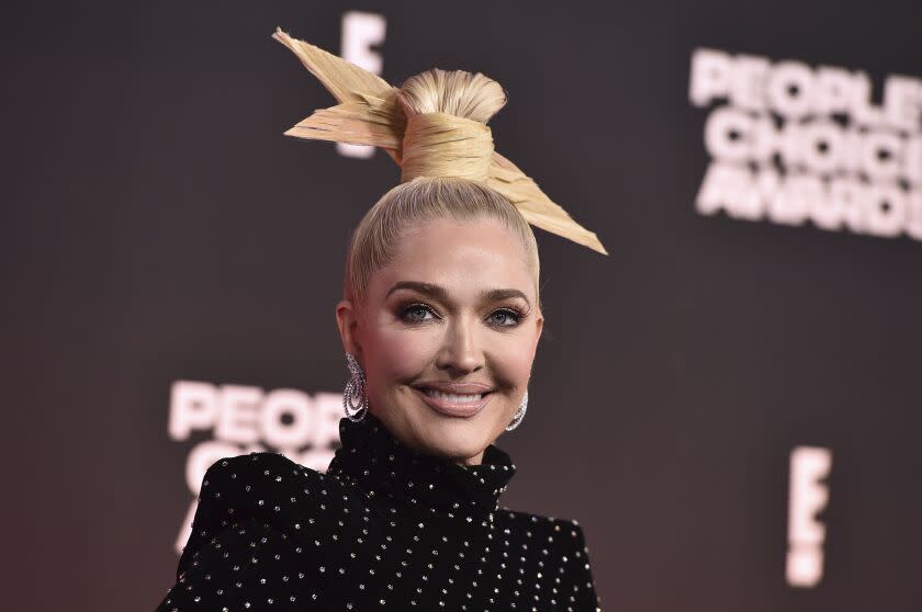 A woman with blond hair in an elaborate updo smiling in a polka-dot turtleneck