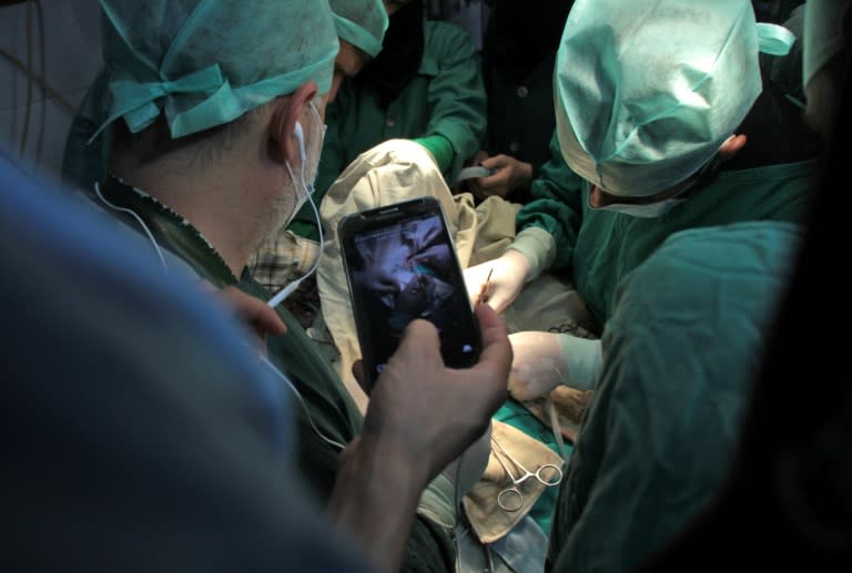 A surgeon holds a cell phone during surgery as he awaits a real-time consultation in Douma, a rebel-held town in the Eastern Ghouta region on October 11, 2017