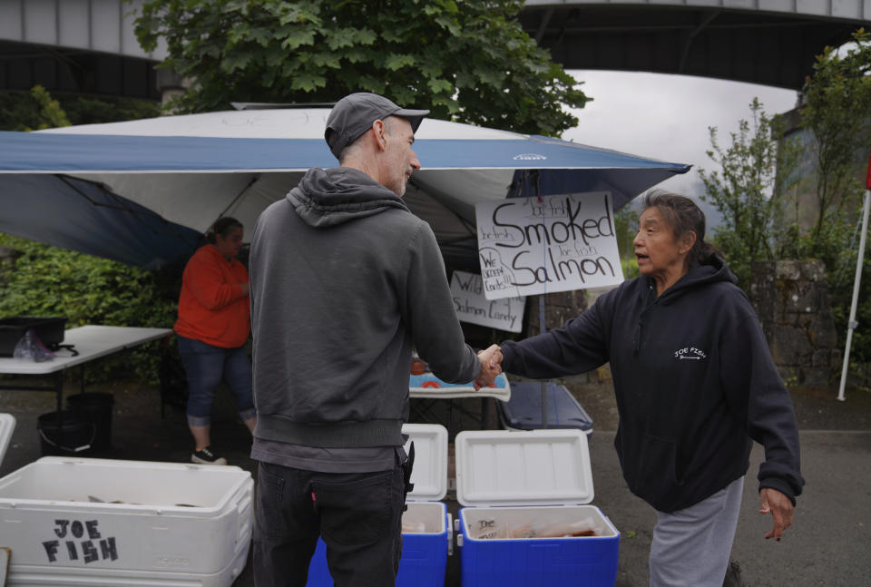 Jared Squires, left, buys fresh salmon from Christy Sampson in a parking lot near the Columbia River on Friday, June 17, 2022, in Cascade Locks, Ore. (AP Photo/Jessie Wardarski)