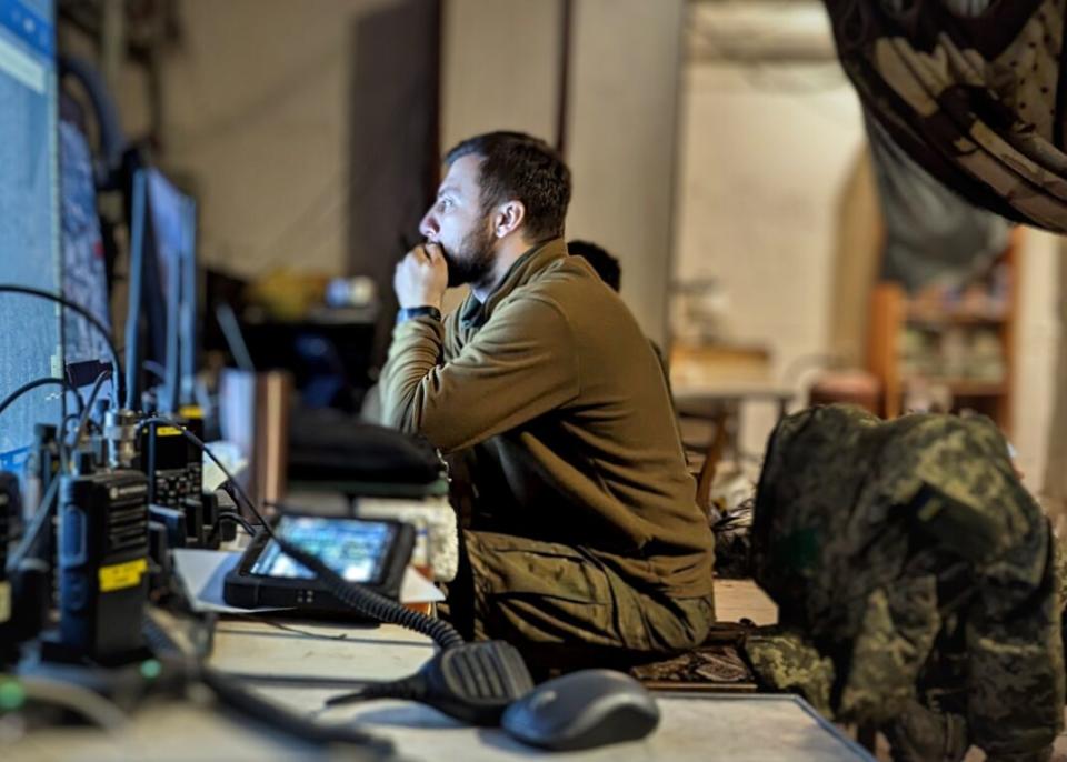 A man in uniform sits at a line of computer screens.