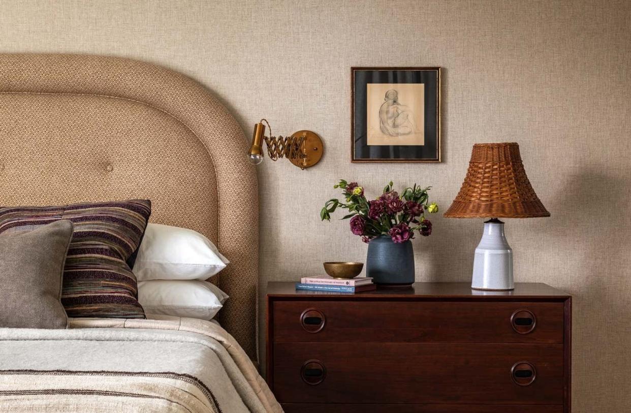  A bedside table styled with lamp, painting, wall light and flowers. 