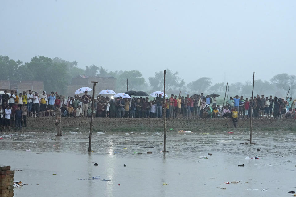 Villagers watch officials visit the site of Tuesday's stampede as it rains in Hathras district, Uttar Pradesh, India, Wednesday, July 3, 2024. Severe overcrowding and a lack of exits contributed to a stampede at a religious festival in northern India, authorities said Wednesday, leaving more than 100 people dead as the faithful surged toward the preacher to touch him and chaos ensued. (AP Photo/Rajesh Kumar Singh)