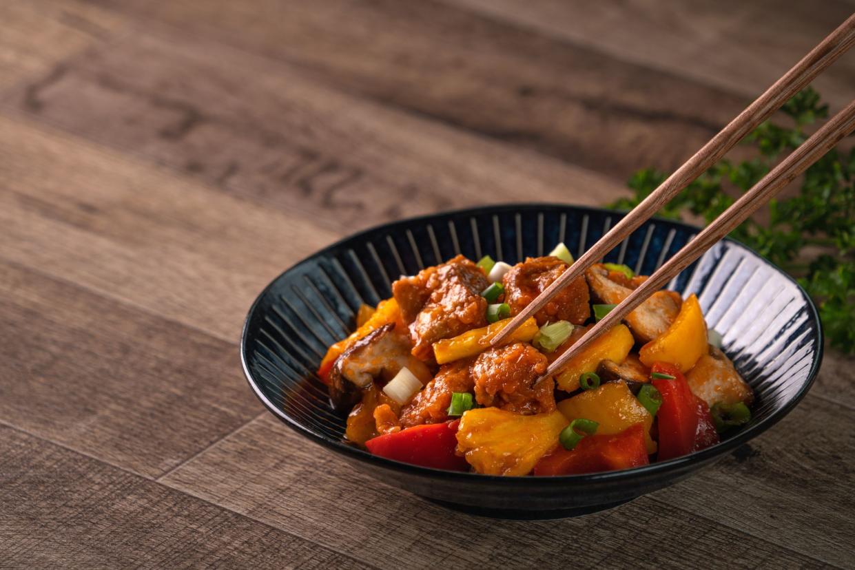 Sweet and sour sauced deep fried pork with chopped pepper and pineapple in a blue plate on wooden table background.