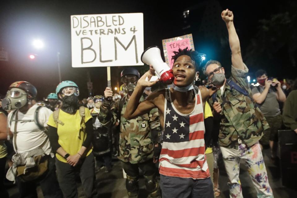 A protester shouts into a bullhorn next to a group of military veterans with a Disabled Veterans 4 BLM sign