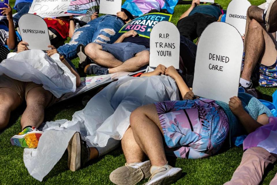 Protesters lie on the ground holding cardboard signs shaped like tombstones in front of the Marriott Fort Lauderdale Airport as the Florida Board of Medicine meets inside. On the agenda is a discussion about a proposed rule by the DeSantis administration to ban doctors from performing gender-affirming surgeries or providing puberty blockers to transgender minors.