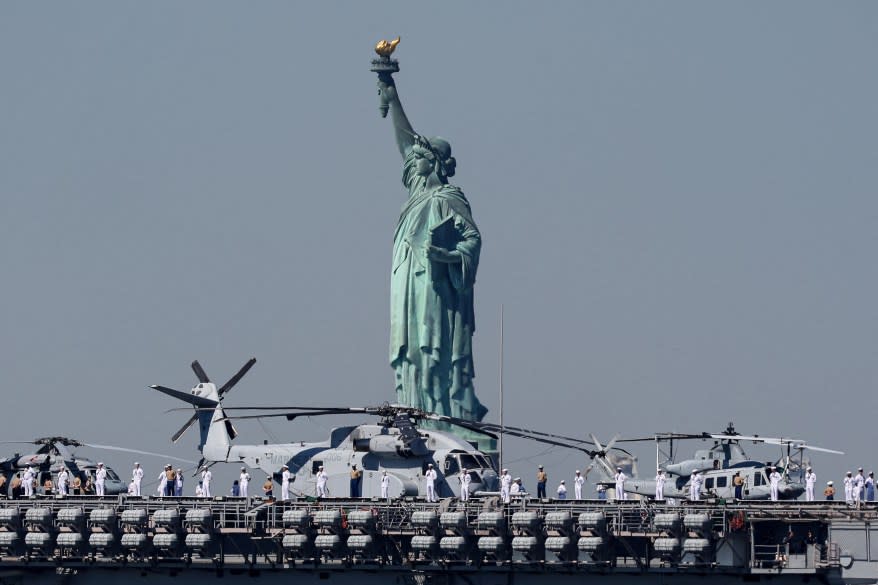 U.S. Sailors and Marines stand on the deck of the USS Bataan as it passes the Statue of Liberty.