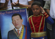 A boy wearing an historical uniform associated with Venezuelan hero Simon Bolivar salutes while standing next to a poster of the late President Hugo Chavez during a military parade commemorating the one year anniversary of Chavez's death, in Caracas, Venezuela, Wednesday, March 5, 2014. The anniversary of Chavez's death was marked with a mix of street protests and solemn commemorations that reflected deep divisions over the Venezuela he left behind. (AP Photo/Fernando Llano)