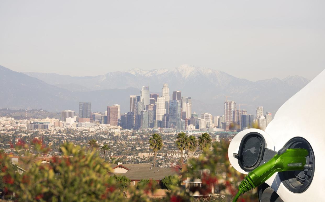 Close up view of Electric Car charging in nature and city view of Los Angeles downtown and houses.