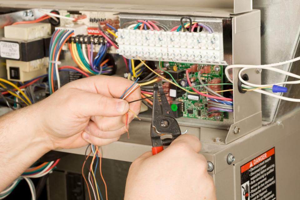 In this close up shot, a pair of hands holding pliers work on wiring in a furnace system.