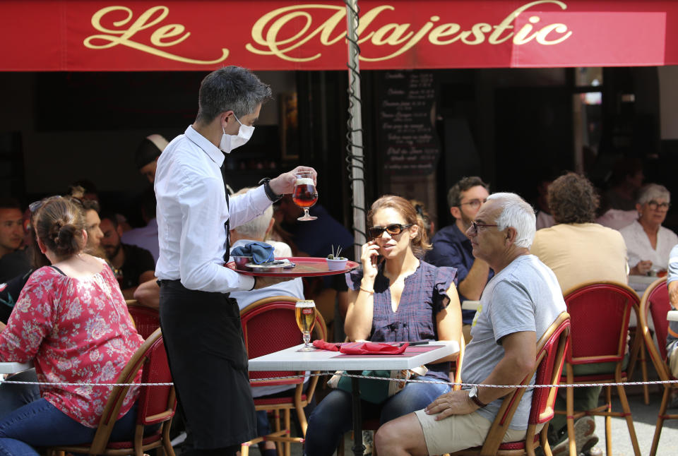 A bartender brings drinks to customers at a cafe in Saint Jean de Luz, southwestern France, Tuesday June 2, 2020. (AP Photo/Bob Edme)