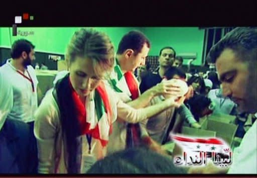 An image grab taken off the official Syrian TV shows President Bashar al-Assad (C) and his wife Asma joining volunteers as they pack boxes at a food distribution center set up at the Al-Fahya stadium in Damascus for victims of fighting in the central restive city Homs