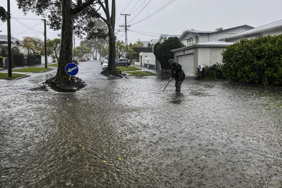 A man attempts to clear a drain in a flooded street in central Auckland, New Zealand, Tuesday, May 9, 2023. Authorities in Auckland have declared a state of emergency as flooding again hits New Zealand's largest city. (Alex Robertson/New Zealand Herald via AP)