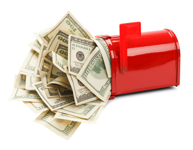 A red mailbox is overflowing with hundred dollar bills that are crammed in it.