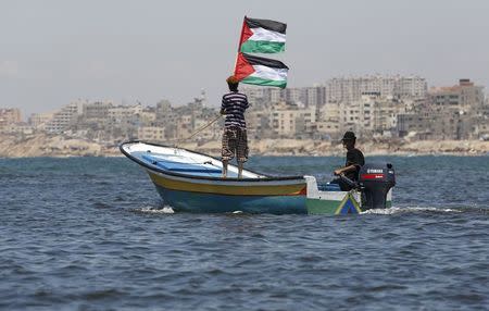 A Palestinian man riding a boat holds Palestinian flags during a protest against the Israeli blocking of a boat of foreign activists from reaching Gaza, at the Seaport of Gaza City June 29, 2015. REUTERS/Suhaib Salem