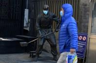 Un hombre con mascarilla pasa por delante de una estatua con mascarilla cerca de la calle peatonal de Qianmen, tras un brote del novedoso coronavirus en el país, en Pekín, China, el 18 de febrero de 2020