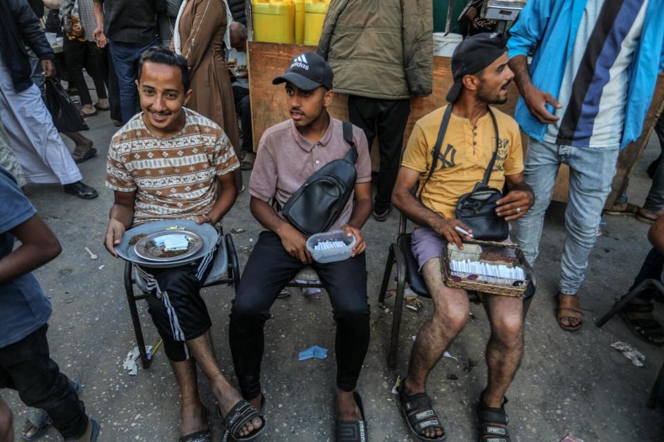 Three seated men hold dishes containing cigarettes