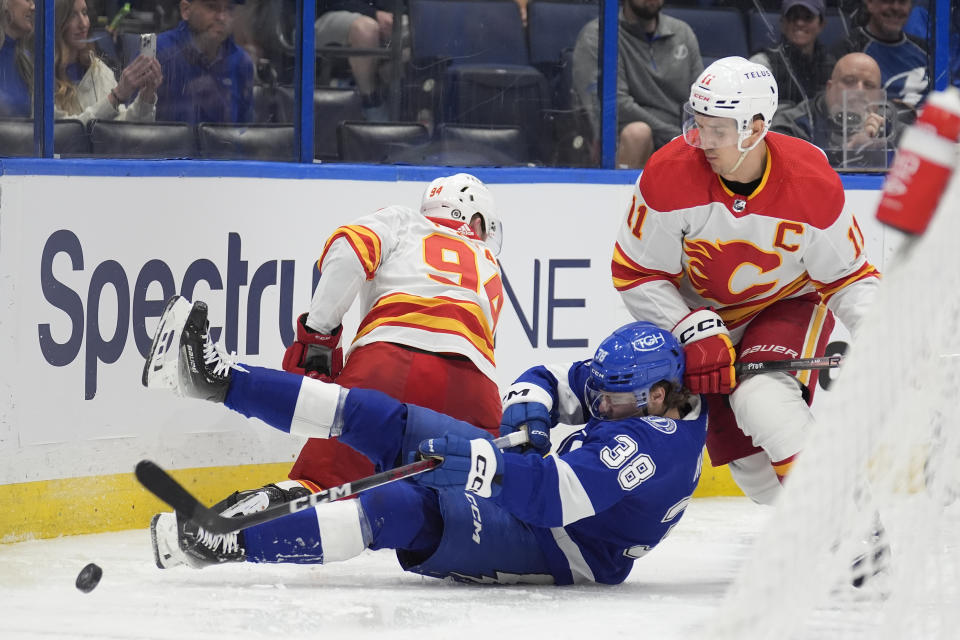 Tampa Bay Lightning left wing Brandon Hagel (38) gets knocked down by Calgary Flames defenseman Brayden Pachal (94) and center Mikael Backlund (11) during the second period of an NHL hockey game Thursday, March 7, 2024, in Tampa, Fla. (AP Photo/Chris O'Meara)